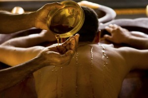 India - Ayurveda - A masseur pours warm oil over a patients body to prepare him for massage